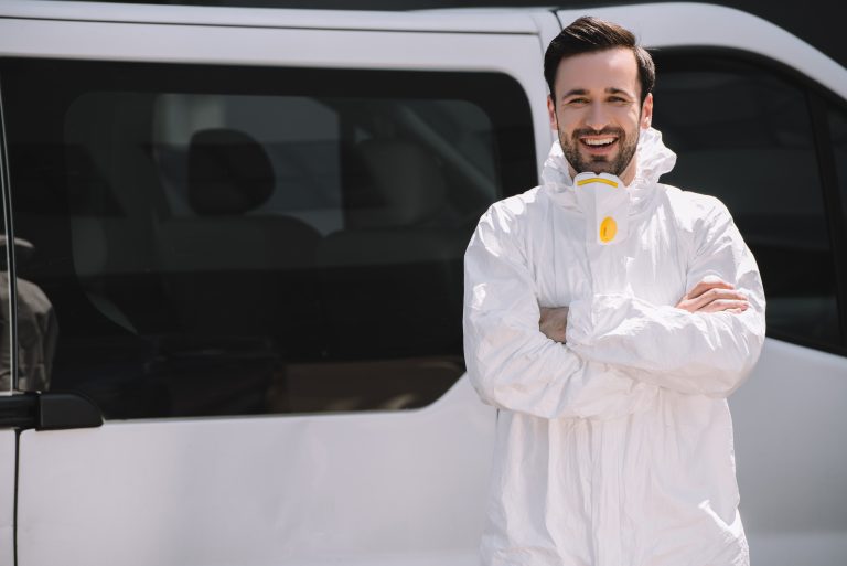 Pest control worker in uniform standing with crossed arms near car on street