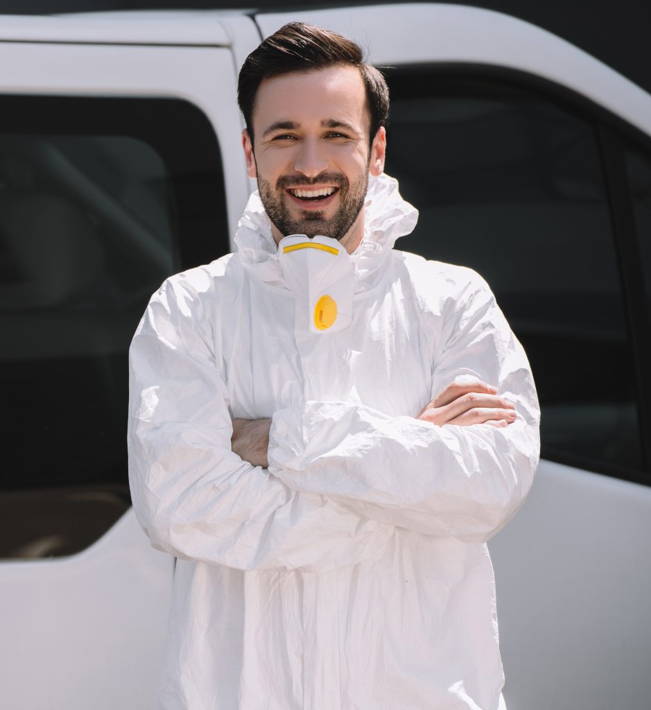 Pest control worker in uniform standing with crossed arms near car on street